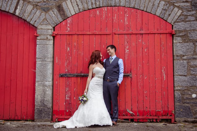 man and wife standing beside red barn door