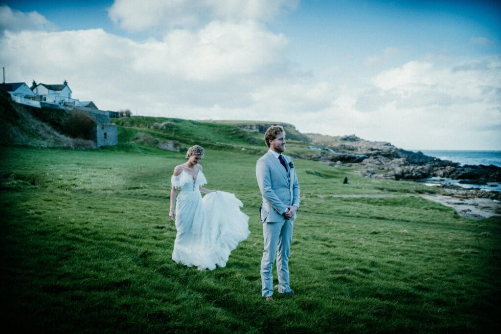 bride and groom firest look brdie stainding behind grrom grren pasture behind her